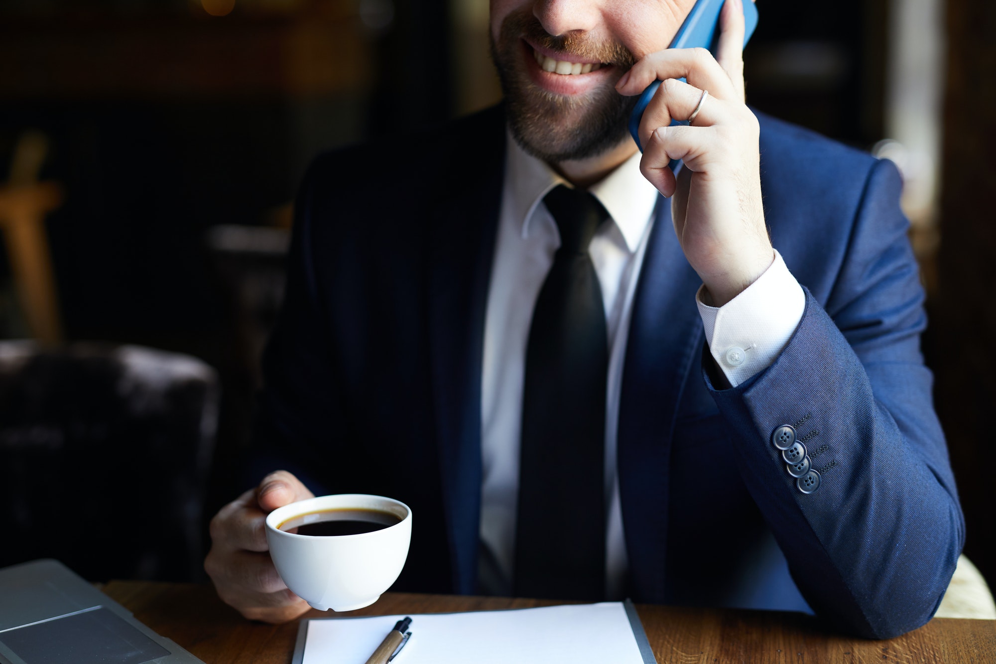 Positive businessman with coffee calling on phone