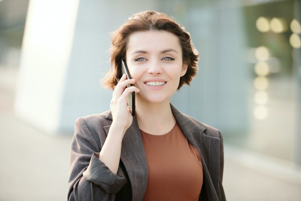 Young smiling brunette businesswoman with smartphone by ear calling client