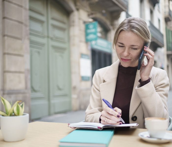 elegant-woman-working-in-a-coffee-shop-writing-on-notebook-and-attending-phone-call.jpg