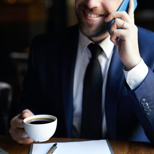 Positive businessman with coffee calling on phone