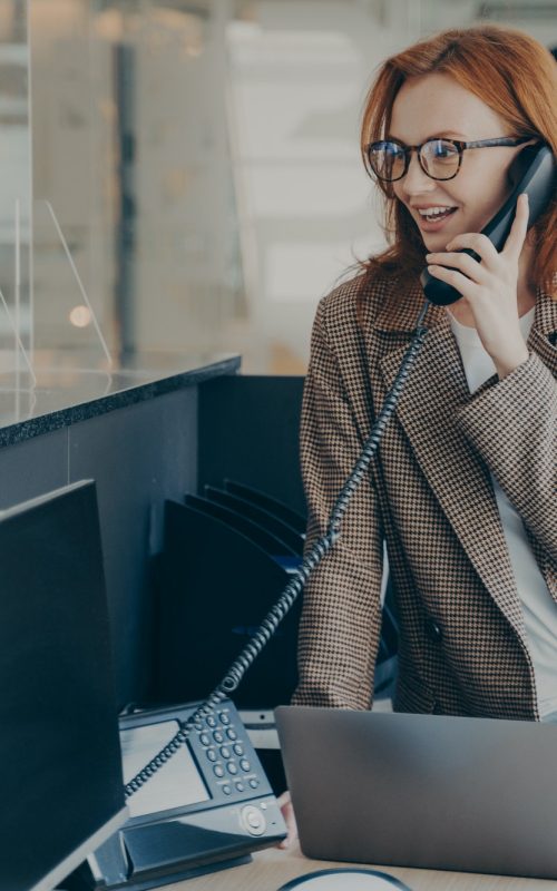 woman-in-spectacles-talking-on-phone-while-sitting-at-her-workplace-in-office.jpg