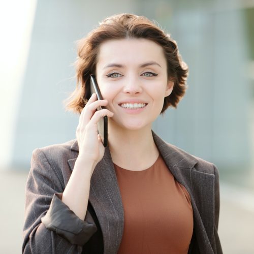 Young smiling brunette businesswoman with smartphone by ear calling client