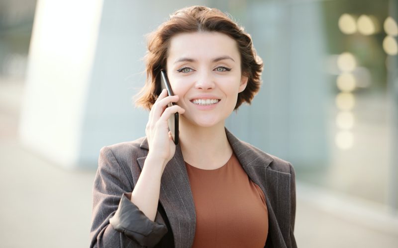 Young smiling brunette businesswoman with smartphone by ear calling client